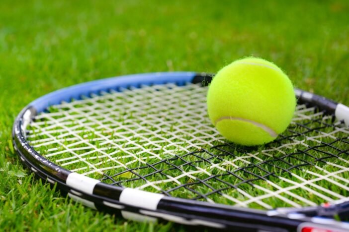 Tennisbal ligt op een tennisracket in het gras.