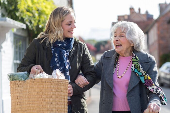Vrouw tilt boodschappen van oudere vrouw.