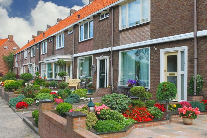 Rijtjes huizen met bloemige voortuinen.