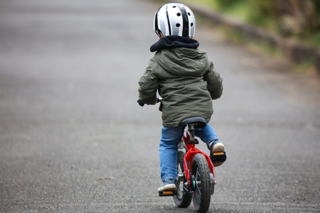 Jong kind is aan het fietsen, we zien hem van de achterkant.