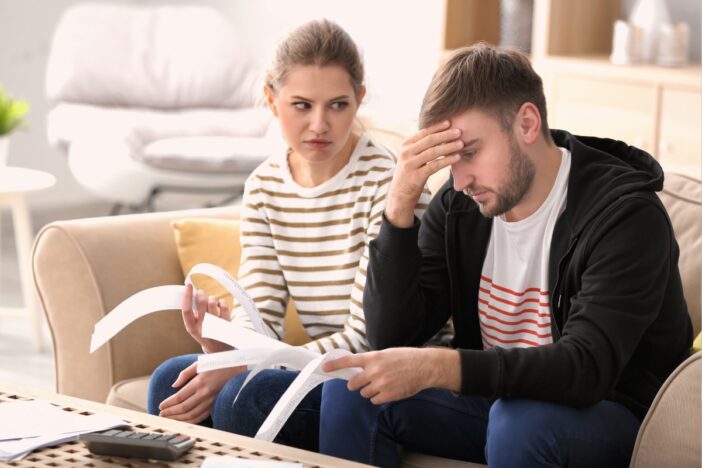 Twee volwassenen hebben onenigheid over geld, ze zitten op de bank met allerlei kassabonnen in hun hand.