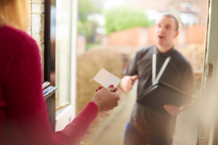 Deurverkoper staat bij vrouw aan de deur.
