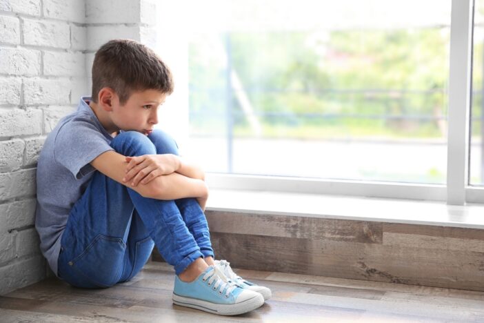Jongen zit met zijn hoofd op zijn knieën droevig voor zich uit te staren.