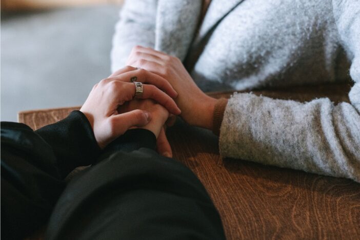 Twee vrouwen aan tafel; ze houden elkaars hand vast.