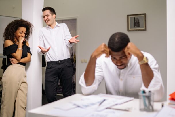 Man en vrouw lachen een collega uit achter zijn rug om.