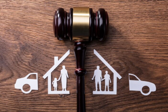 Illustratie van een rechtershamer op een houten tafel, met daarbij getekend een door de helft gedeeld huis en auto. Symboliek voor een scheiding.