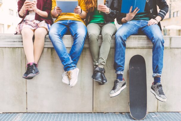 Vier tieners zitten op een stenen randje met hun tablet of smartphone in de hand.