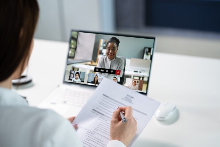 Vrouw beeldbelt via laptop met een andere vrouw en maakt aantekeningen op papier.