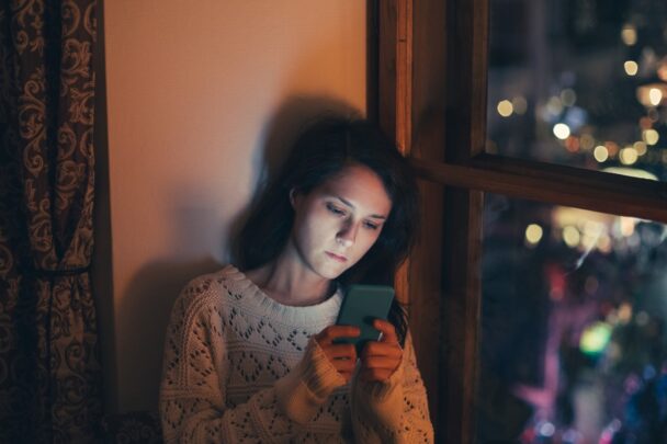 Vrouw gebruikt mobiele telefoon bij raam.