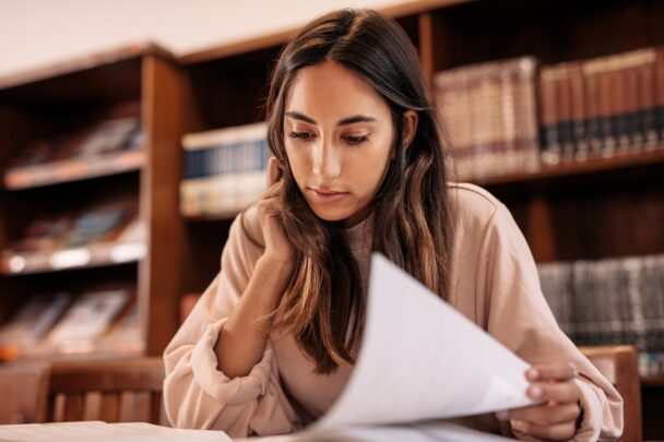 Vrouw bekijkt papieren. Achter haar zie je een boekenkast vol boeken.