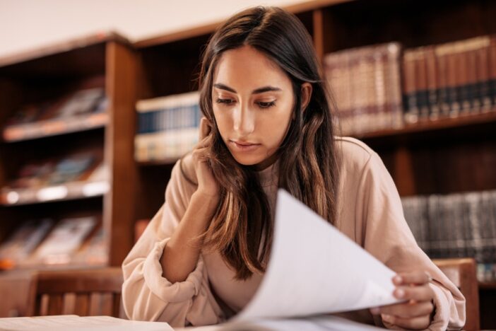 Vrouw bekijkt papieren. Achter haar zie je een boekenkast vol boeken.
