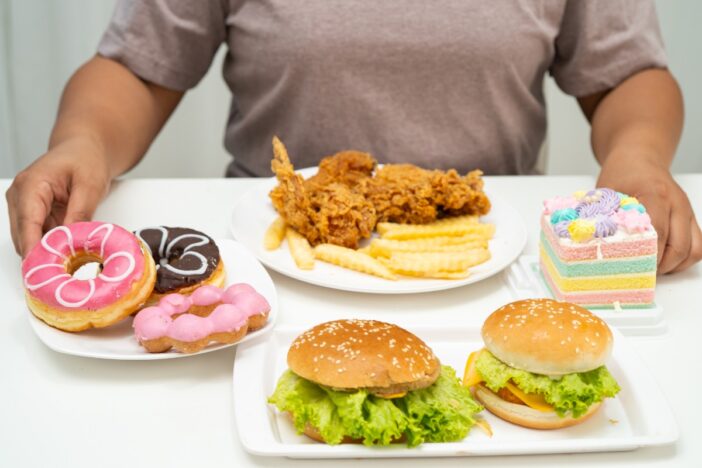 Man zit aan tafel met aantal borden met junkfood, zoals hamburgers en donuts.