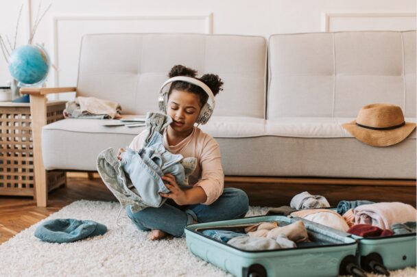Klein meisje heeft kleding in haar handen die ze haalde uit een koffertje.