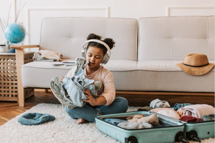Klein meisje heeft kleding in haar handen die ze haalde uit een koffertje.
