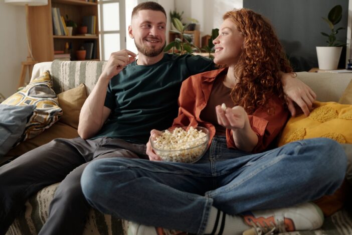Man en vrouw zitten samen op de bank met een bak popcorn.
