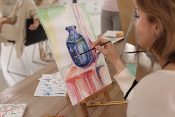 Vrouw schildert een donkere vaas op een canvas.