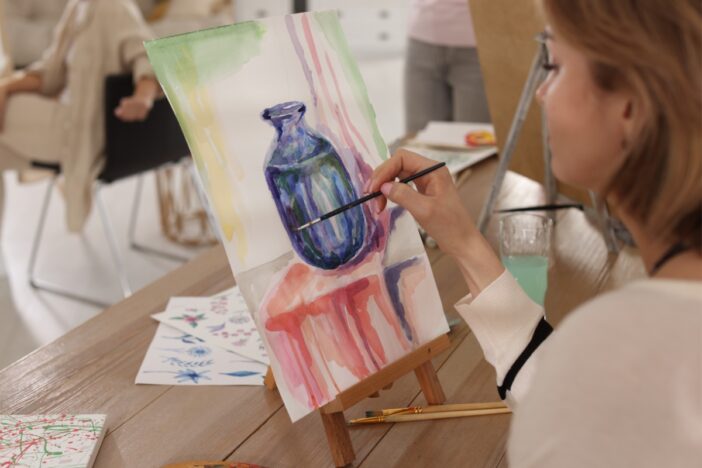 Vrouw schildert een donkere vaas op een canvas.