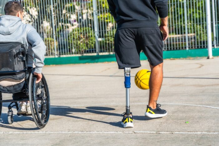 Man met beenprothese en man in rolstoel spelen basketbal.