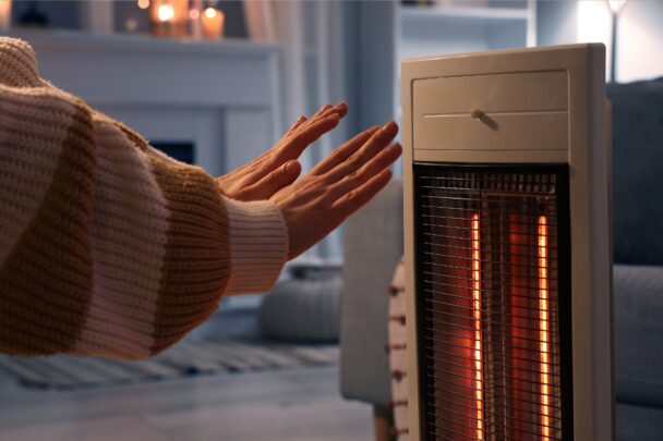 Vrouw warmt haar handen aan een elektrisch kacheltje.