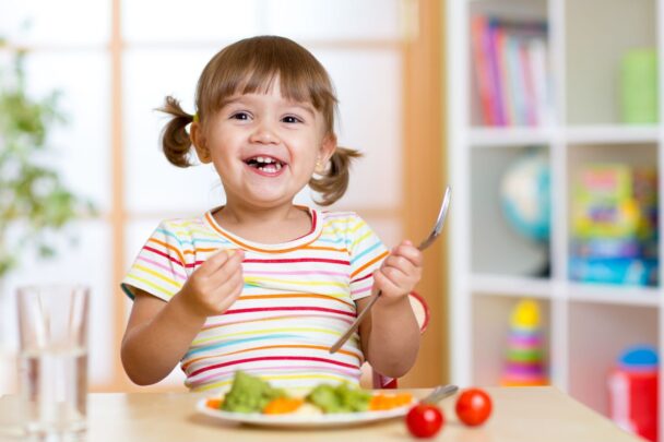 Peutermeisje eet een bordje fruit leeg en lacht breeduit.