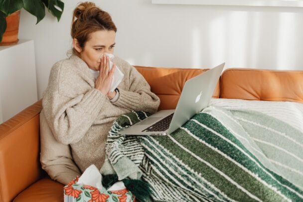 Vrouw zit verkouden en snotterend met zakdoekjes op de bank.