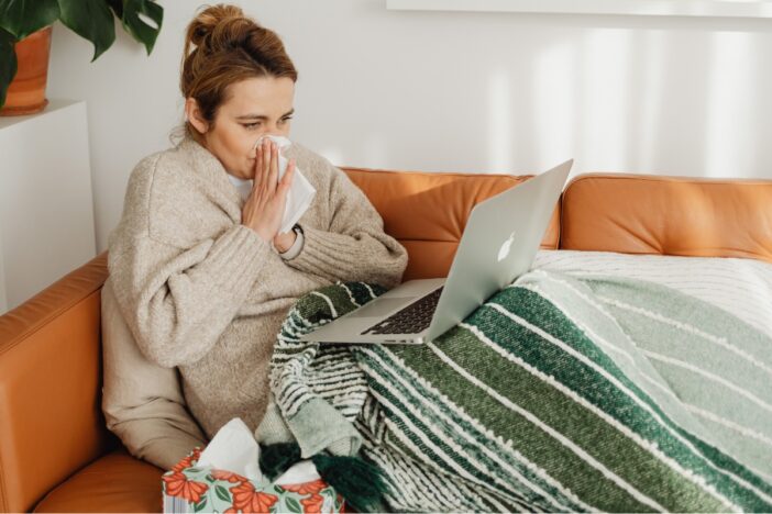 Vrouw zit verkouden en snotterend met zakdoekjes op de bank.