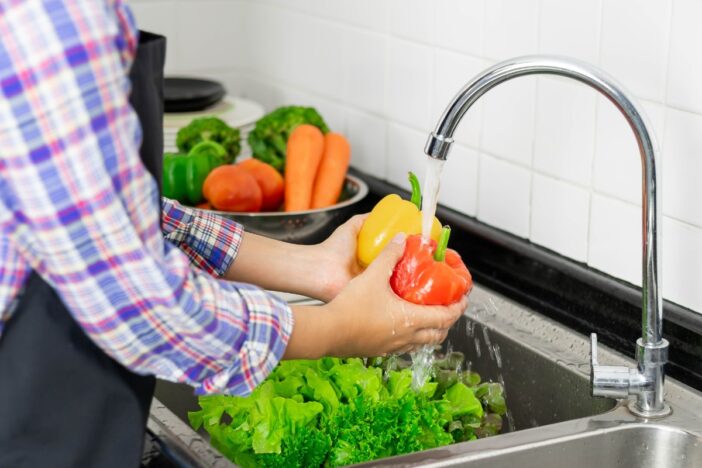 Persoon wast groenten onder de kraan.
