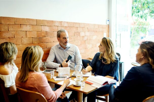 Vijf mensen zitten aan tafel te praten en wat te drinken.
