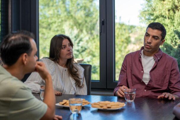 Twee mannen en een vrouw zitten aan tafel in gesprek met elkaar.