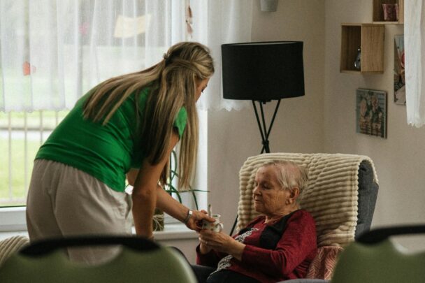 Jonge vrouw helpt oudere vrouw die in een stoel zit en houdt hand vast.