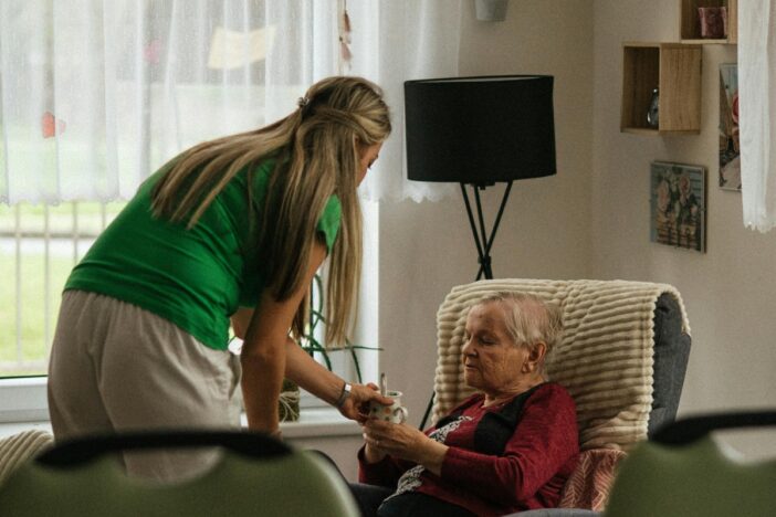Jonge vrouw helpt oudere vrouw die in een stoel zit en houdt hand vast.