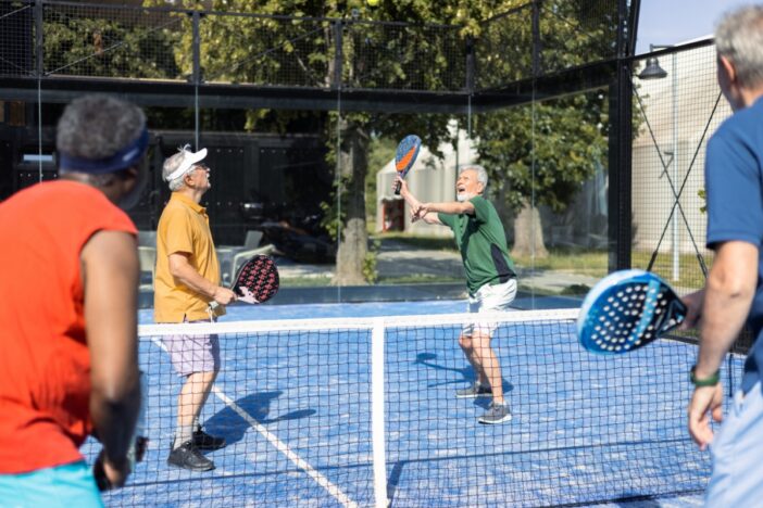 Groepjevan vier mannen is aan het padellen in de zonnige buitenlucht.
