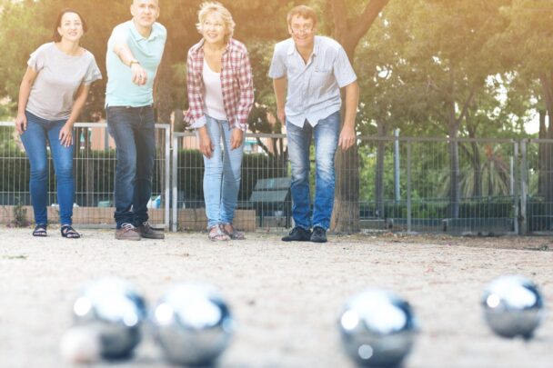 Vier mensen spelen petanque op een baan van zand.