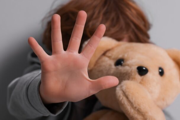 Kindje met teddybeer maakt een stopgebaar met zijn hand.