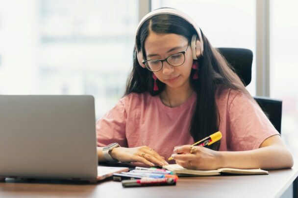 Jonge vrouw met bril en koptelefoon op is aan het studeren.