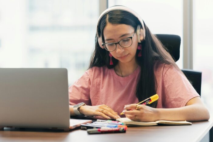 Jonge vrouw met bril en koptelefoon op is aan het studeren.