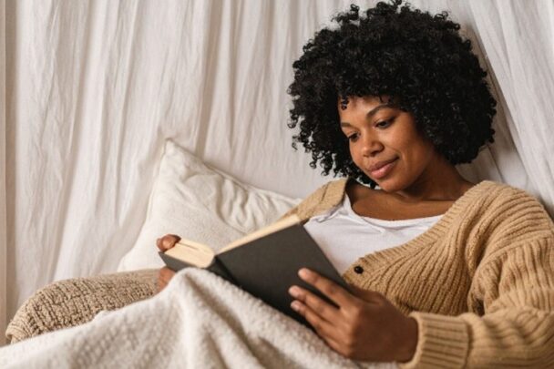 Vrouw leest een boek en zit onder een dekentje.