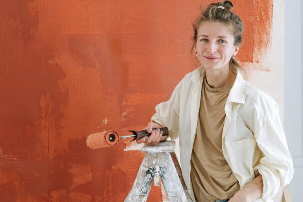 Vrouw staat met verfroller voor een net geschilderde muur.