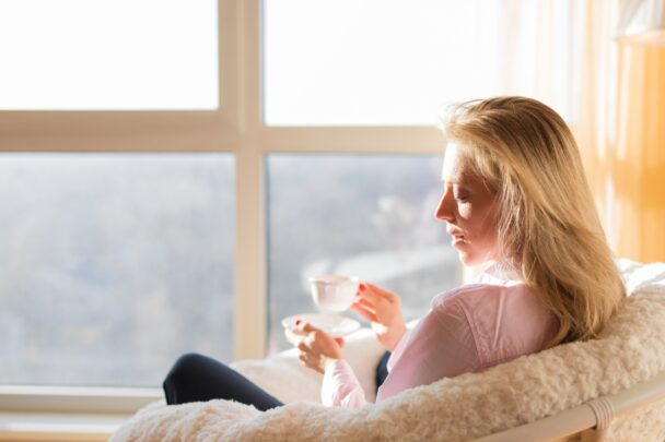 Vrouw zit in huis in het zonlicht met een kopje thee.