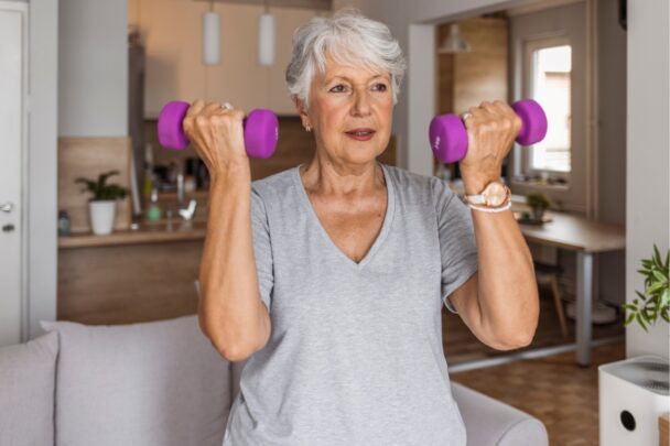 Oudere vrouw traint met dumbbells in huis.