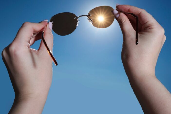 Vrouwenhanden houden zonnebril voor de zon, tegen een helderblauwe lucht.