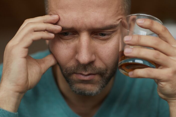 Man heeft glas alcohol in zijn handen en oogt droevig.