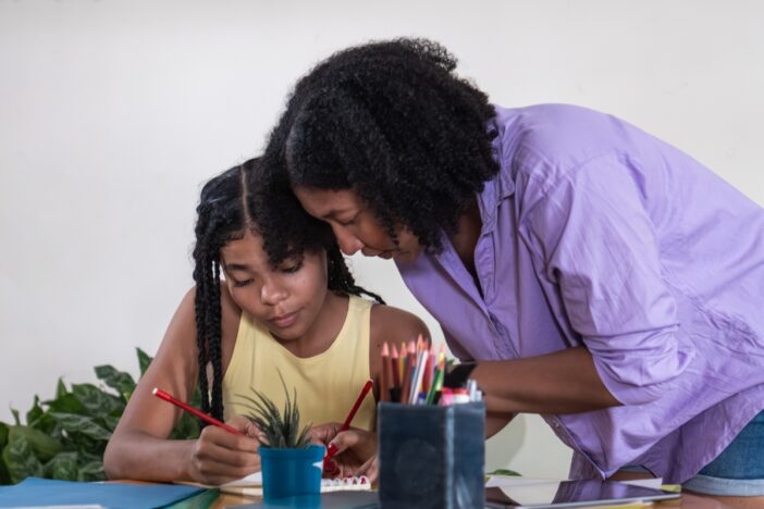 Moeder helpt haar dochter die aan tafel zit en aan het tekenen is.
