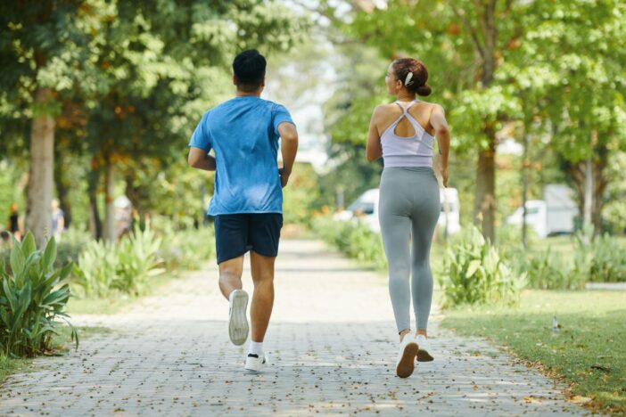 Man en vrouw joggen samen in een bomenlaan.