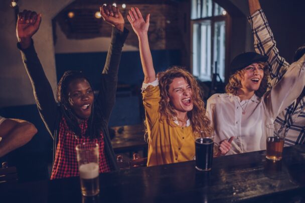 Drie vrouwen zitten blij aan een bar met drankjes voor zich.