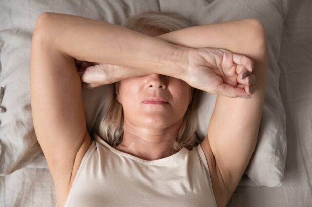 Slapeloze vrouw kruist haar armen voor haar gezicht terwijl ze in bed ligt.