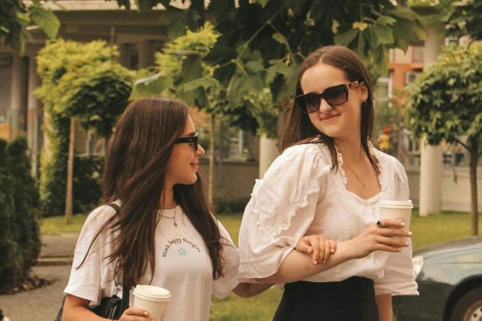 Twee wandelende meisjes met koffie in handen.