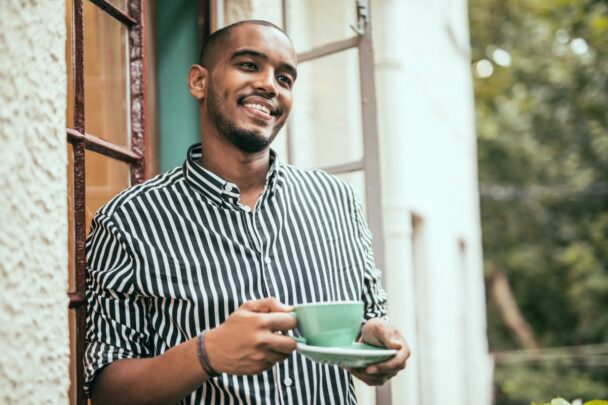 Man staat met kopje koffie in de hand in zijn deuropening naar buiten te kijken.