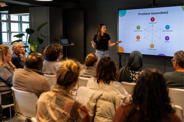 Groep mensen volgt een presentatie van een spreker over positieve gezondheid.
