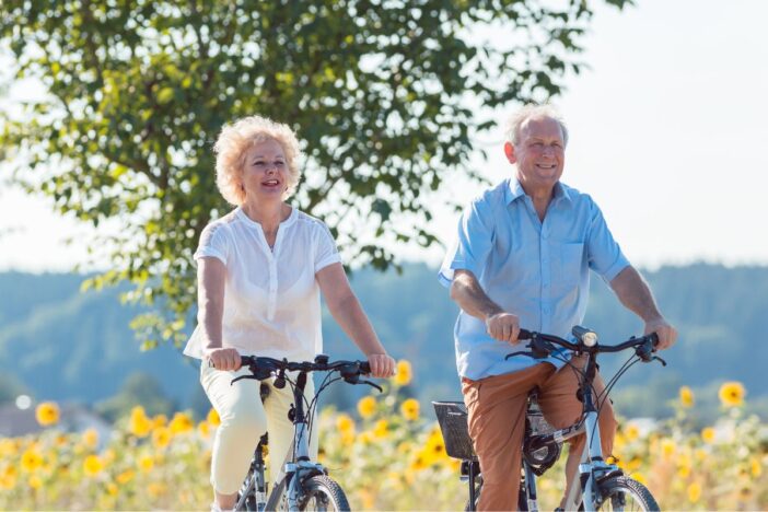 Ouder stel fietst samen langs zonnebloemenveld.